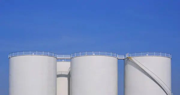 Row of white storage fuel tanks group in oil industrial refinery area against blue sky background