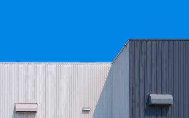 Gri ve beyaz alüminyum kıvrımlı fabrika binası. Kurutucu menfezleri mavi açık gökyüzü arka planına karşıdır.