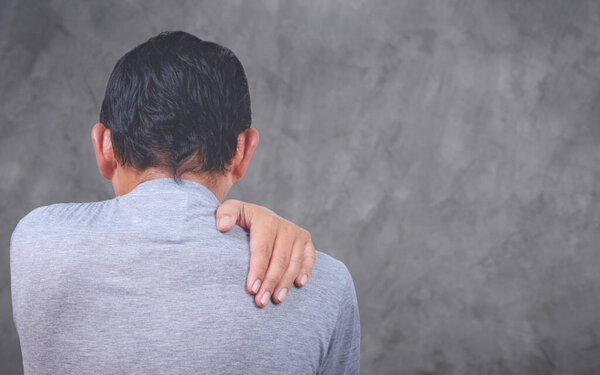 Middle aged man has shoulder pain with blurred gray cement wall background, health problem concept, rear view with copy space