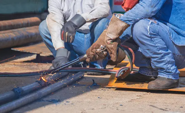 Cropped image of 2 welders using acetylene gas welding torch machine to welding galvanized steel pipes in construction site