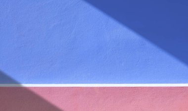 Renkli mavi ve pembe dış çimento duvar arka planı, yüzeyde köşegen güneş ışığı ve gölge desenleri olan minimal tarzda.