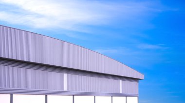 Mavi gökyüzü arka planına karşı alüminyum duvarda eğri çatılı ve daha yüksek havalandırmalı büyük bir sanayi deposu.