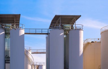 Petrol endüstrisi fabrikasının rafineri bölgesinde mavi gökyüzü arka planına karşı depolama yakıt tanklarına sahip kimyasal silolar ve boru hattı sistemi.