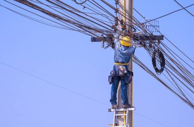 Merdivende güvenlik ekipmanı olan elektrikçi elektrik direğine bağlantı kurmak ve bağlantıyı kesmek için anten yerleştiriyor.