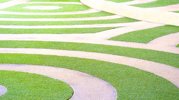 stock image Geometric curve lines pattern of artificial green turf and exposed aggregate finish cobblestone pavement floor decoration in public park area