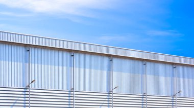 Büyük sanayi deposu, yağmur oluğu ve yağmur suyu drenaj boru hatları, alüminyum duvarda LED güneş duvarı lambaları, mavi gökyüzü arka planı, perspektif yan görünümü.