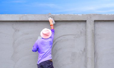 İnşaat işçisi beton duvar yapısına çimento yapıştırıyor.