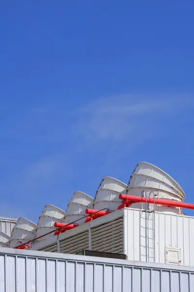 Stock image Row of white ventilation chimneys and exhausting machine in HVAC system on rooftop of factory building against blue sky background in vertical frame