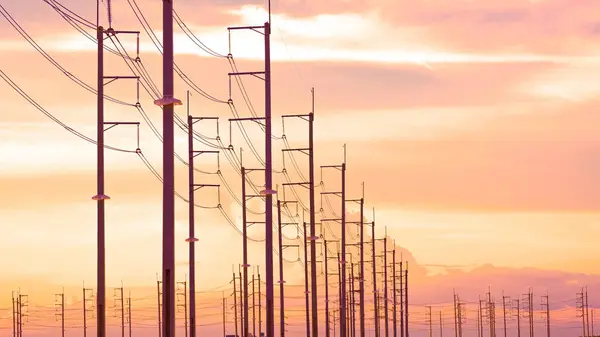 Stock image Silhouette row of many electric poles with cable lines in industrial settlement area against orange clouds with golden sunlight on sunset sky background in evening time