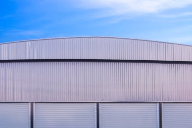 Gri alüminyum eğimli çatısı ve mavi gökyüzü arka planına karşı 4 otomatik kapağı olan büyük bir sanayi deposu.