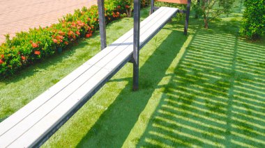 Kamu parkının bahçesindeki yeşil çimenlikte uzun beyaz ahşap bank