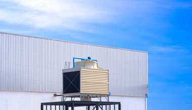 Fabrika binasının dışındaki metal askı üzerinde kare soğutma kulesi mavi gökyüzü arka planına karşı, kopya alanı ile perspektif yan görünümü