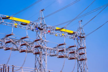 Yalıtımlı yüksek voltajlı elektrik direkleri ve mavi gökyüzü arka planına karşı elektrik dağıtım hattının kablosu.