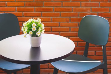 Güzel yapay Oxeye Papatya çiçekleri siyah yuvarlak ahşap sehpanın üzerinde beyaz vazoda eski kahve dükkanındaki tuğla duvarın yanında.