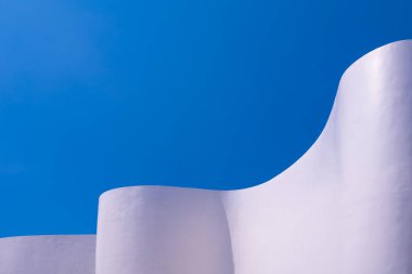 Mavi gökyüzü arkaplanına karşı minimal tarzda beyaz eğimli beton bina duvarı, soyut modern mimari tasarım, düşük açı ve perspektif kenar görünümü