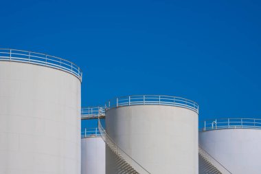 Petrol sanayi rafinerisindeki ham petrol tankları grubuna karşı mavi berrak gökyüzü arkaplanı, düşük açılı fotokopi alanı