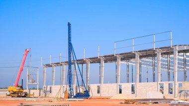 Mavi gökyüzü arka planına karşı inşaat alanında büyük endüstriyel fabrika yapı yapısına sahip yığın makinası ve vinç kamyonu.