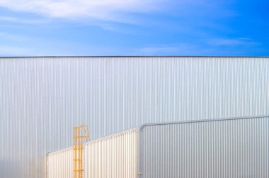 Mavi gökyüzü arka planına karşı alüminyum kıvrımlı çelik duvarlı sabit merdiveni olan sanayi fabrikası binası.