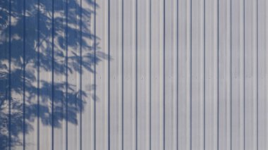 Yüzeyinde ışık ve ağaç dalı gölgesi olan depo evinin gri kıvrımlı çelik duvar arka planı