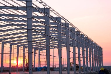 Gün batımına karşı inşaat alanında fazla mesai yapan işçiyle fabrika yapı iskeleti.