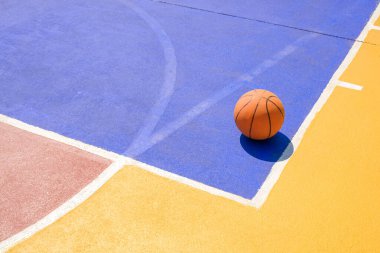 Basketball on outdoors basketball court with colorful pattern on concrete yard floor surface