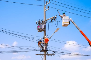 Vinç kamyonlu elektrikçiler, mavi gökyüzü arka planına karşı elektrik direğine düşük açılı ekipman kuruyor.