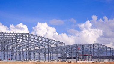 İnşaat alanındaki iki fabrika fabrikasının büyük metal yapısı mavi gökyüzü arka planındaki bulutlara karşı, yan görüş.