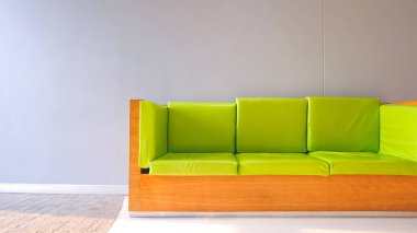 Kireç yeşili yastıklı ahşap kanepe gri tahta duvarın önünde arka planda beyaz mermer ve bej taş döşemeli modern oturma odasının içinde minimal tarzda.