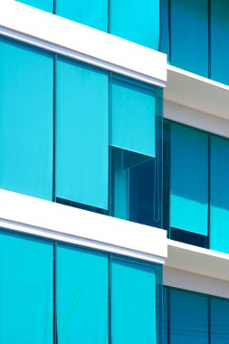 Mavi tekerlekli güneşli modern ofis binası, cam duvarın içinde dikey çerçevede jaluzi, dış mimari arka planı minimal biçimdedir.