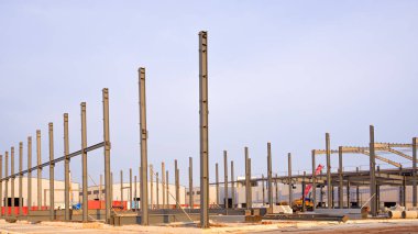 Mavi gökyüzü arka planına karşı yeni fabrika şantiye alanındaki endüstriyel depo binasının metal kolon yapısı.