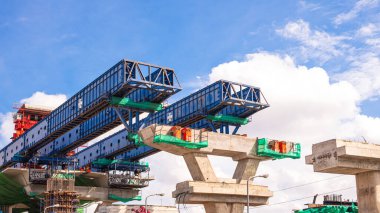 Mavi gökyüzü arkaplanına karşı yüksek karayolu inşaatında beton tipik segment birleşimi kurmak için gantry metal yapısı başlatılıyor. Kopya alanı ile düşük açı görünümü
