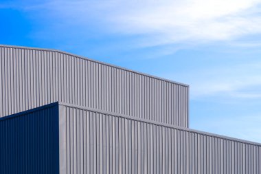 Mavi gökyüzü zeminine karşı gri alüminyum kıvrımlı metal duvarı olan fabrika deposu. Kopya alanı olan düşük açı manzaralı.