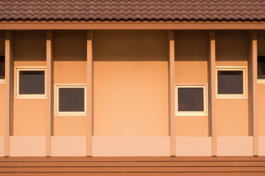 Kahverengi kiremit çatılı bej bir bina ve soyut geometrik desenli gölgeleme yüzgeçleri ve beton duvar yüzeyindeki kare renkli camlı pencereler. Klasik ev dış mimari arka planı