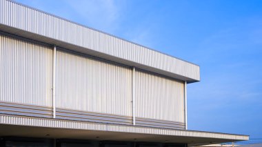Depo endüstriyel fabrika binası alüminyum yağmur suyu çıkışlı ve gümüş kıvrımlı metal duvarda havalandırma hoparlörü mavi gökyüzü arka planına karşı, perspektif yan görünümü