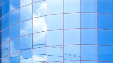 Yüzeyinde mavi gökyüzü yansıması olan modern eğri cam ofis duvarı, minimal tasarım arka planında dış mimari