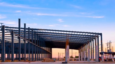 İnşaat alanında metal kolonlar ve çatı kiriş iskeletine sahip siluet fabrikası yapı akşam gökyüzü arkaplanına karşı, fotokopi alanı ile ön manzara