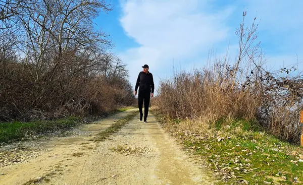 stock image A man dressed in black walks along a rural road at early spring season