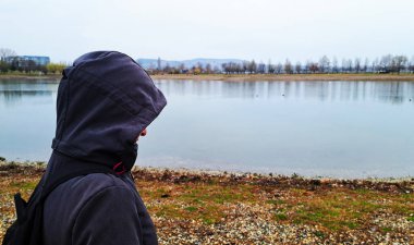 Kapüşonlu bir kadın gölün kıyısında duruyor.