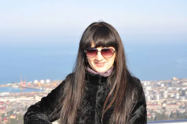 Uzun saçlı ve güneş gözlüklü bir kadın balkonda dikiliyor.