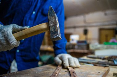 Bir adam atölyede çekiçle çalışır..
