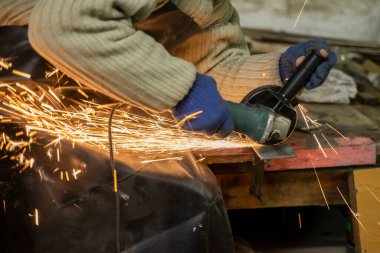 Özel giysiler içindeki çilingir, prodüksiyonda çalışıyor. Açı öğütücüyle metal işleme. Metal işçiliğinde kıvılcımlar.