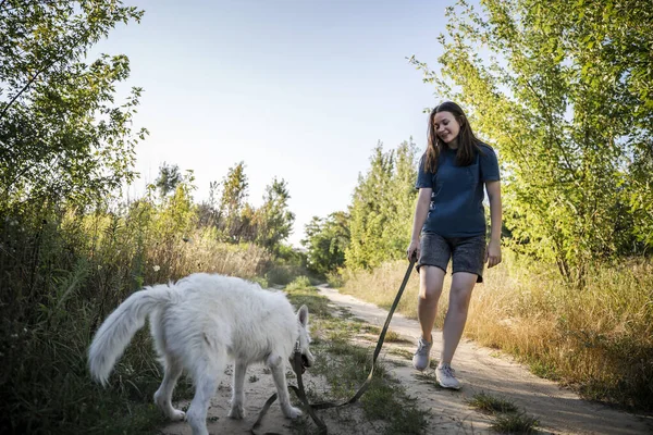Bir kız gün boyunca beyaz bir köpeği gezdirir. Ormanın arka planındalar..