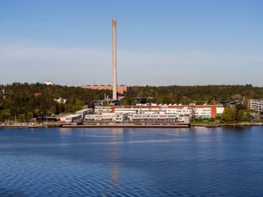 Rıhtımın yanındaki büyük, modern, düşük Bonver lojistik sanayi binası. Bir yaz günü mavi gökyüzünün altında görünen uzun bir bacası var. Denizden bakıldığında arazi sık ormanlık alanın önüne kurulmuştur..