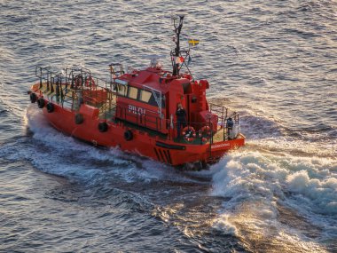 Turuncu boyalı pilot gemisi Stockholm Takımadaları 'nda bir yolcu gemisine eşlik ettikten sonra gemideki mürettebattan birinin yolcu gemisini çekerek eve doğru yola çıkıyor..