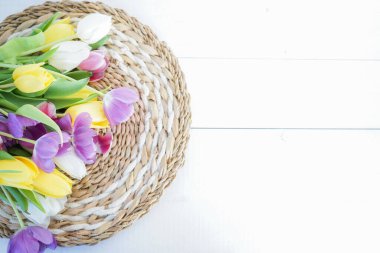 Beyaz ahşap zemin üzerinde sarı, mor ve beyaz laleler.