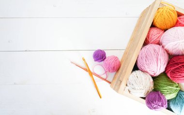 Beyaz ahşap zemin üzerinde ahşap bir kutuda pastel renkli yün toplar, pembe, sarı ve beyaz yazı arkaplanı için boşluk