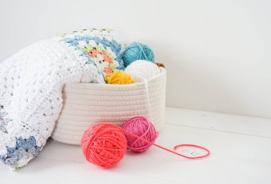 Beyaz ahşap zeminde yün topları olan beyaz sepetli büyük anne battaniyesi.