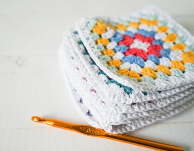 Tığ işi kancası ve beyaz ahşap el yapımı ahşap zemin olan çok renkli büyükanne kareleri.