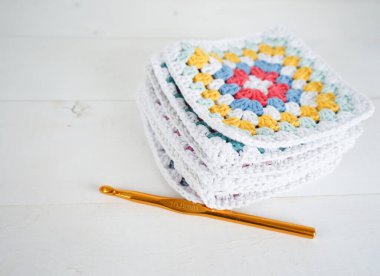 Tığ işi kancası ve beyaz ahşap el yapımı ahşap zemin olan çok renkli büyükanne kareleri.