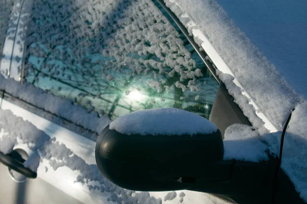 A car in the snow. The window reflects the sky and the sun. Close up